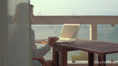 高级妇女使用笔记本电脑坐在桌子上的户外阳台与观海她上网冲浪使用